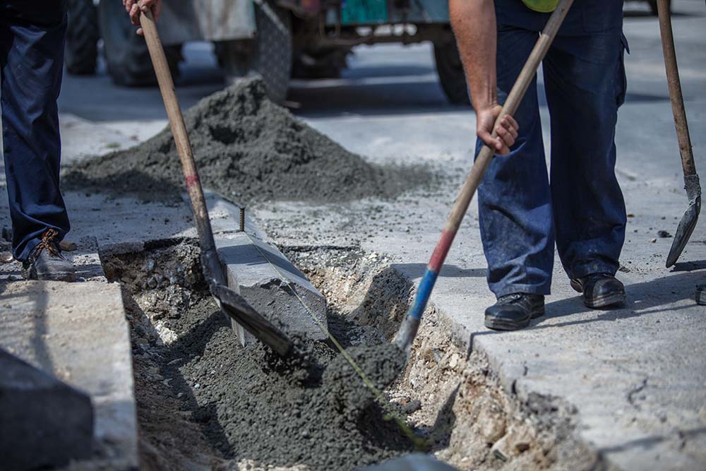 Concrete driveway construction in progress — freshly poured concrete being leveled and finished by contractors, with formed edges and a smooth surface ready for curing.